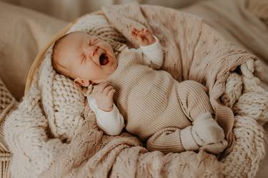 Gähnendes Baby in einem mit Decken ausgelegten Babykorb