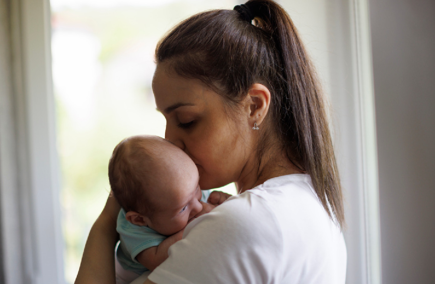 Junge Mutter hält ihr Baby auf dem Arm und küsst es