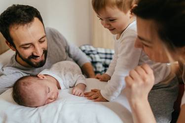 Eltern mit schlafendem Baby und lächelndem Kleinkind im Bett