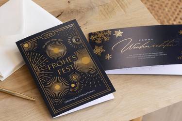 Geschäftliche Weihnachtskarten mit Folienveredelung und Kuverts auf einem Tisch.