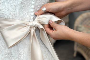Nahaufnahme weibliche Hände beim Biden einer Satinschleife am Hochzeitskleid
