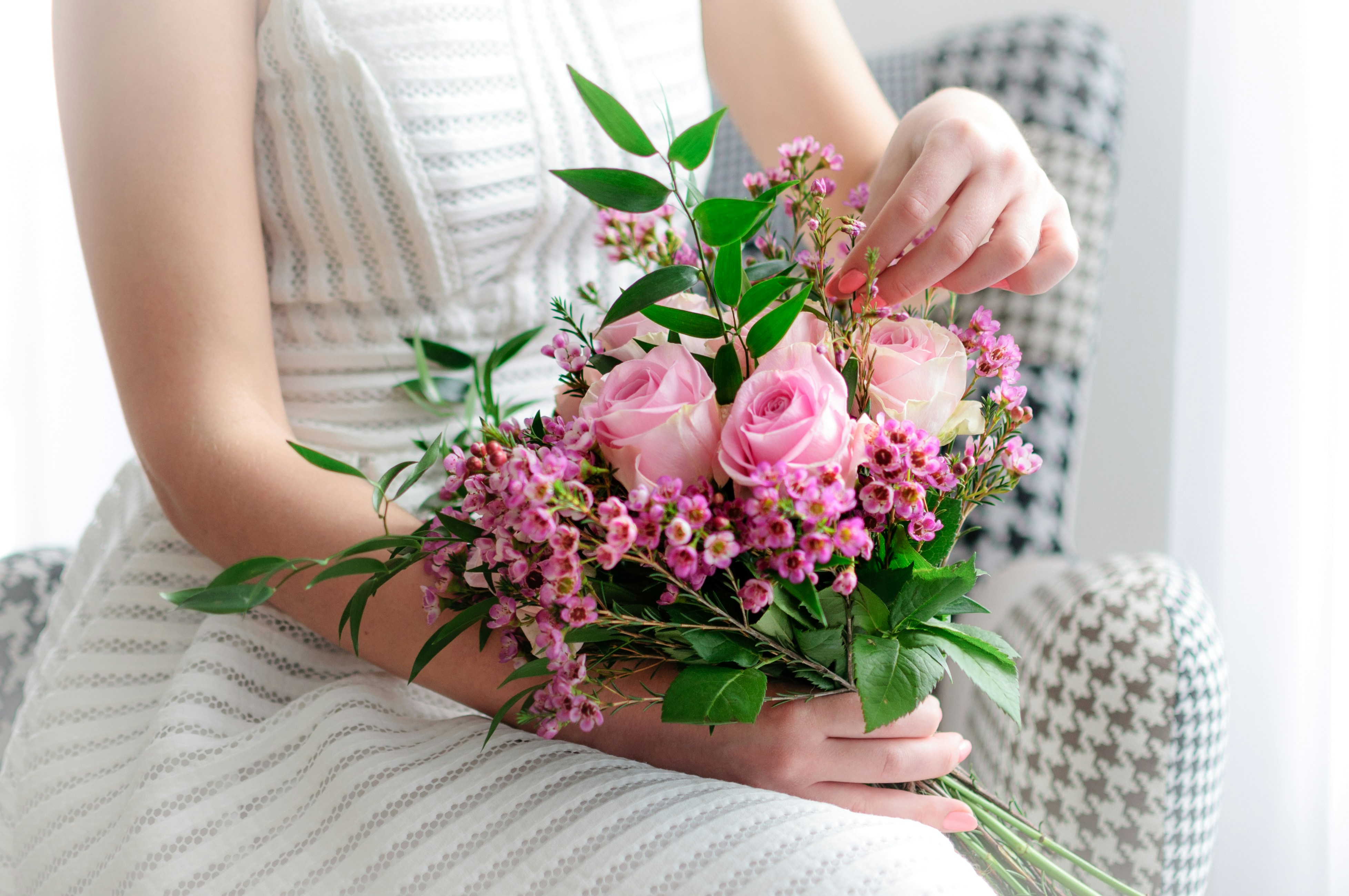 Frau sitzt in weißem Kleid mit einem Strauß rosa Blumen