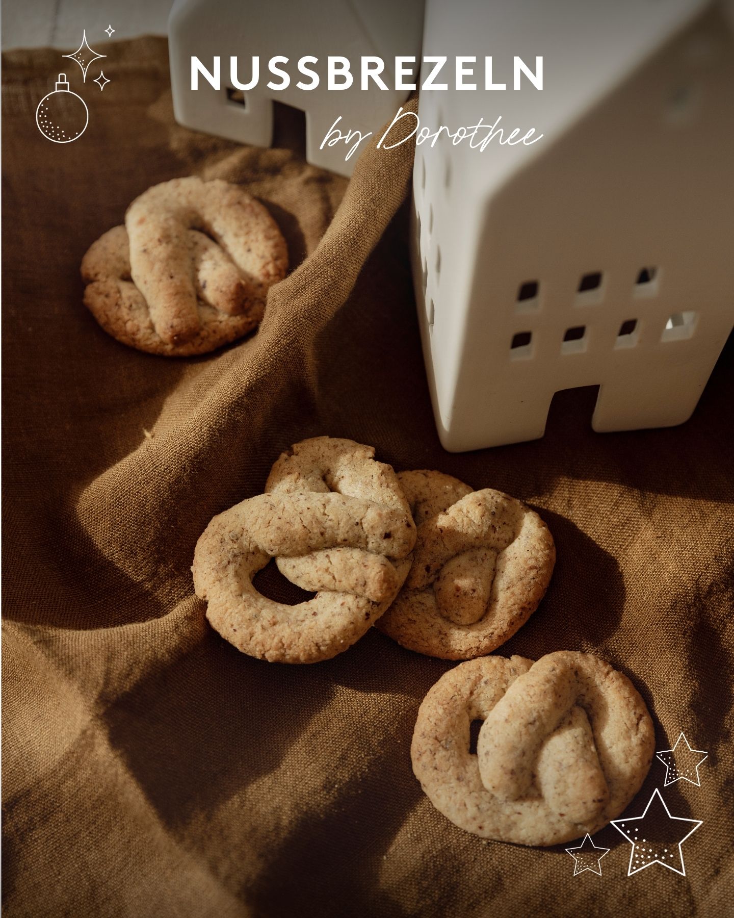 Hellbraun gebackene Weihnachtsplätzchen mit weißen Keramikhäusern auf braunem Leinentuch dekoriert